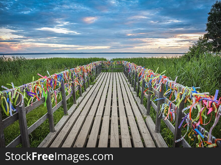 Bridge on the lake with colorful ribbons, bridge at sunset, colorful ribbons on the railing of the bridge