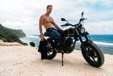 Portrait Of Sexy Athletic Man With Naked Torso Near Custom Motorbike, Ocean At Background Stock Photo