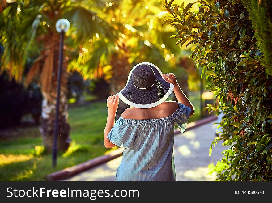 Young beautiful woman in beach hat walking under tropical palm trees at sunny day in Bodrum, Turkey. Vacation Outdoors Seascape