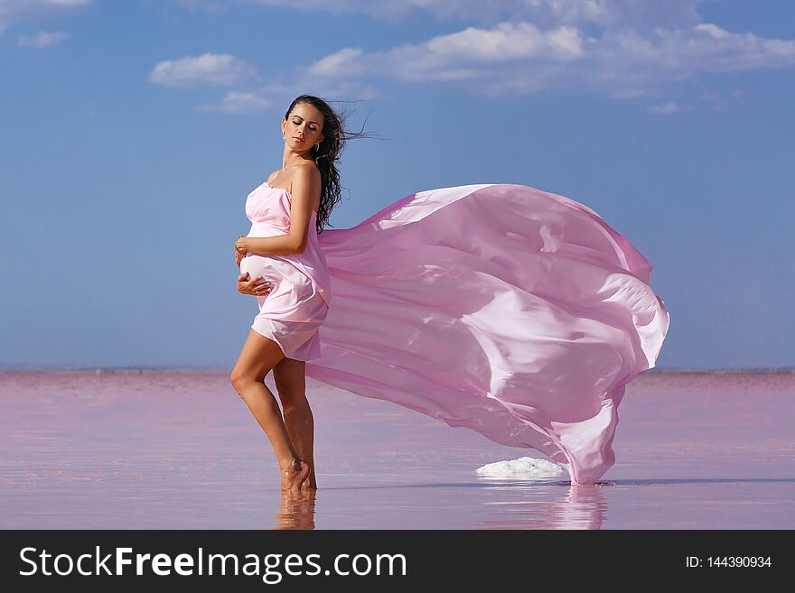 Beautiful young pregnant woman enjoying the sun on the beach, pink lake