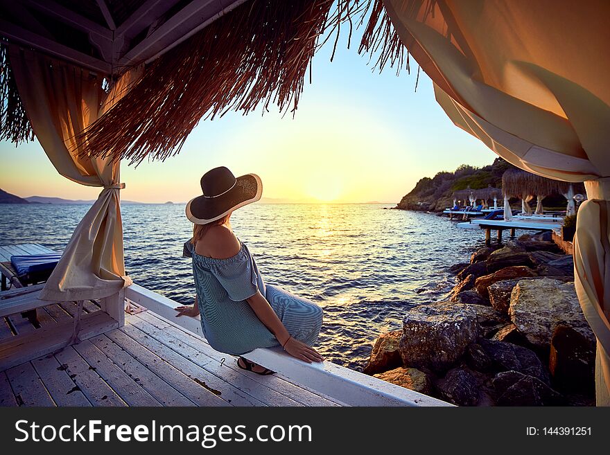 Woman in hat relaxing by the sea in a luxurious beachfront hotel resort at sunset enjoying perfect beach holiday vacation in