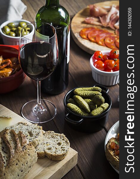 Wine and tapas dishes on a wooden table. Dishes include garlic prawns, bread and cheese, meat and charcuterie, toasts, tomatoes, olives, gherkins and red wine