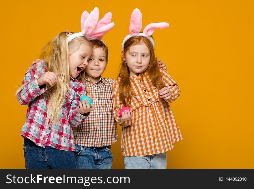 Two little girls and boy with Easter bunny ears holding colorful eggs