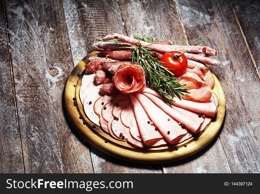 Food tray with delicious salami, pieces of sliced ham, sausage and salad. Meat platter with selection on table