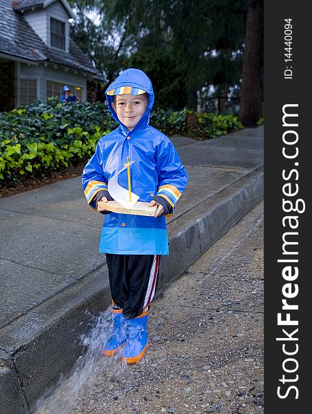 Young boy playing with toy boat in the rain wearing rain slickers and golashes. Young boy playing with toy boat in the rain wearing rain slickers and golashes.