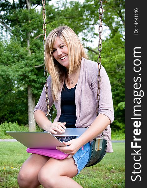 Attractive young teenager sits in a swing with her laptop. Attractive young teenager sits in a swing with her laptop.