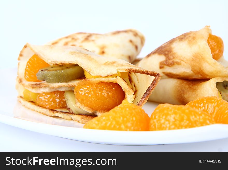 Pancakes stuffed with fruit (peach, kiwi, mandarin) on a plate decorated with fruit