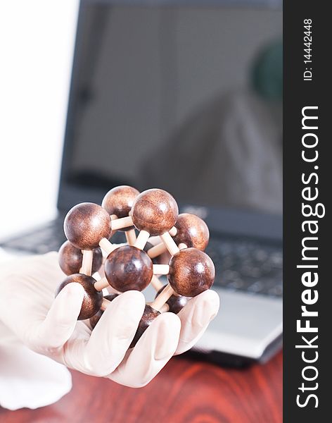 Holding molecule with gloves and laptop in the background