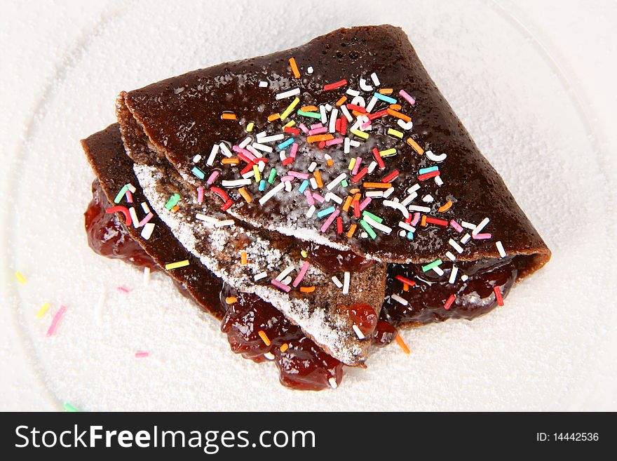 Chocolate pancake stuffed with strawberry jam covered with caster sugar and colorful sprinkles. Chocolate pancake stuffed with strawberry jam covered with caster sugar and colorful sprinkles