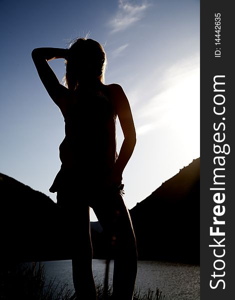A silhouette of a woman in front of some water with her arm up. A silhouette of a woman in front of some water with her arm up.