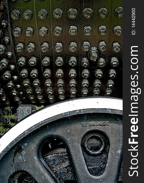 Many bolts on a black iron surface with iron wheel in foreground. Many bolts on a black iron surface with iron wheel in foreground.