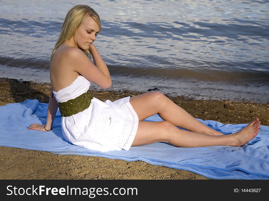 A beautiful woman sitting on a blue blanket on the beach relaxing. A beautiful woman sitting on a blue blanket on the beach relaxing.