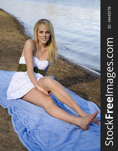 A beautiful woman sitting on a blue blanket on the beach relaxing. A beautiful woman sitting on a blue blanket on the beach relaxing.