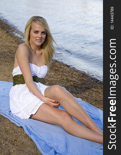 A beautiful woman sitting on a blue blanket on the beach relaxing. A beautiful woman sitting on a blue blanket on the beach relaxing.