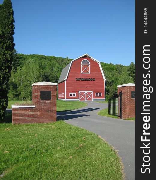 An open gate leads to a red barn and the fields beyond. It's a tranquil setting with bright blue sky and the afternoon sunshine.