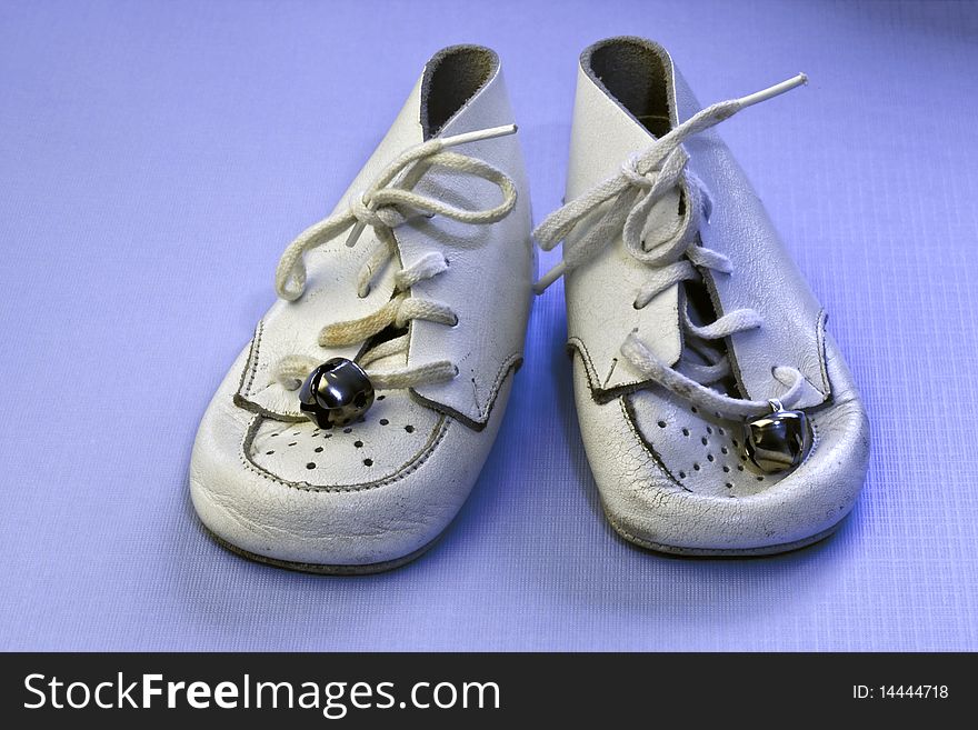 Vintage soft white leather baby shoes on an isolated blue background. Vintage soft white leather baby shoes on an isolated blue background