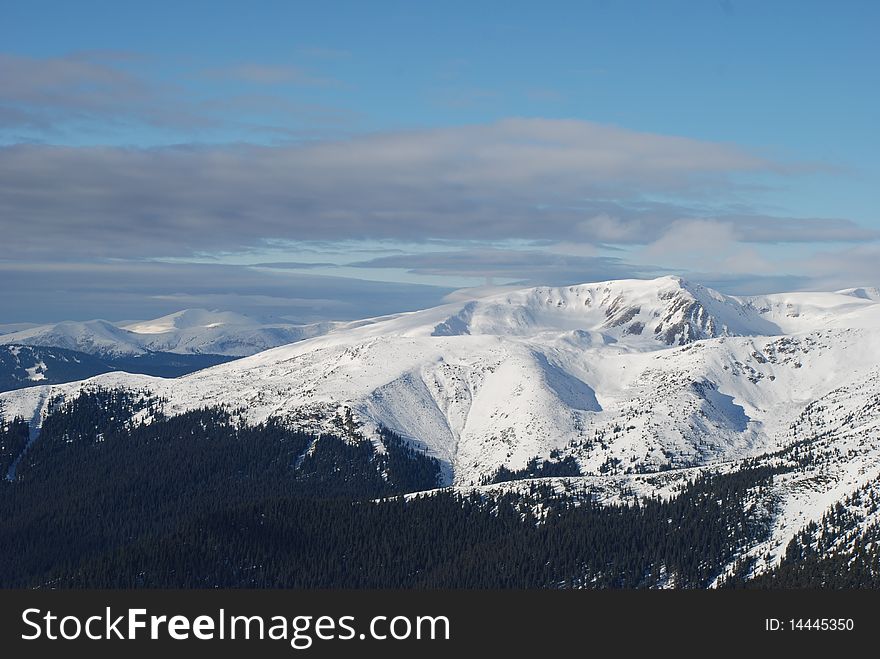 A winter landscape with mountain tops under clouds. A winter landscape with mountain tops under clouds.