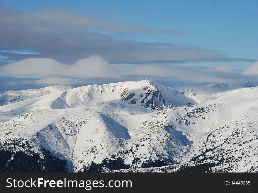 A winter landscape with mountain tops under clouds. A winter landscape with mountain tops under clouds.