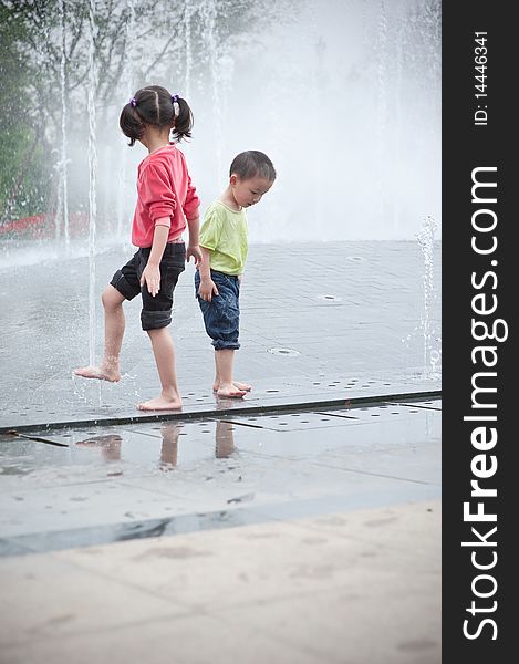 Asian boy and girl play by fountain