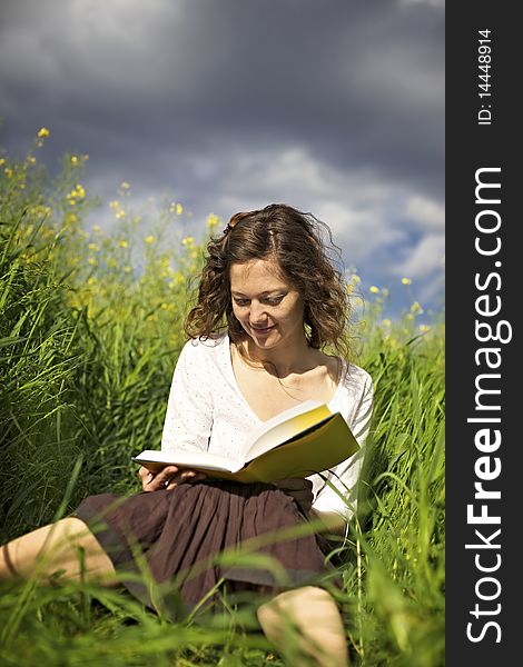 Young smiling woman sitting in green field and reading a book. Young smiling woman sitting in green field and reading a book.