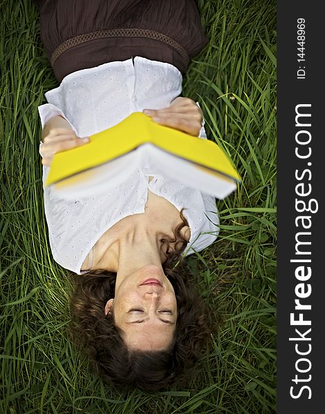 Young smiling woman lying in meadow and reading a book, top view. Young smiling woman lying in meadow and reading a book, top view.