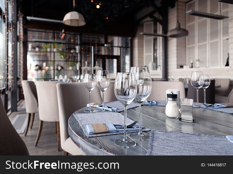 Restaurant interior, serving, wine and water glasses, plates, forks and knives on textile napkins stand in row on vintage gray wooden table. Concept banquet, birthday, conference, group lunch. Restaurant interior, serving, wine and water glasses, plates, forks and knives on textile napkins stand in row on vintage gray wooden table. Concept banquet, birthday, conference, group lunch