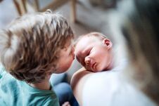 A Small Boy Kissing A Sleeping Newborn Baby Brother At Home. Stock Photo