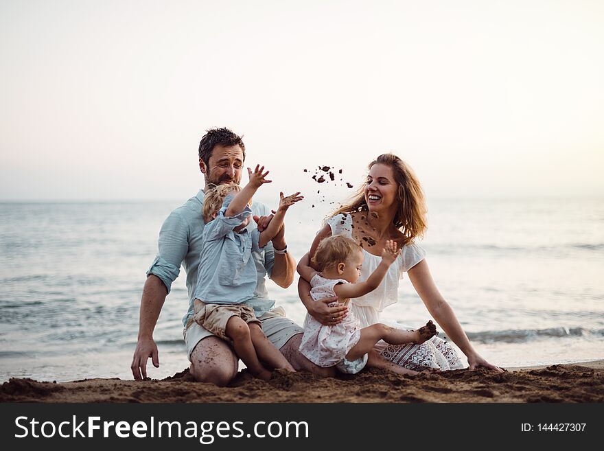 A Family With Two Toddler Children Sitting On Sand Beach On Summer Holiday.