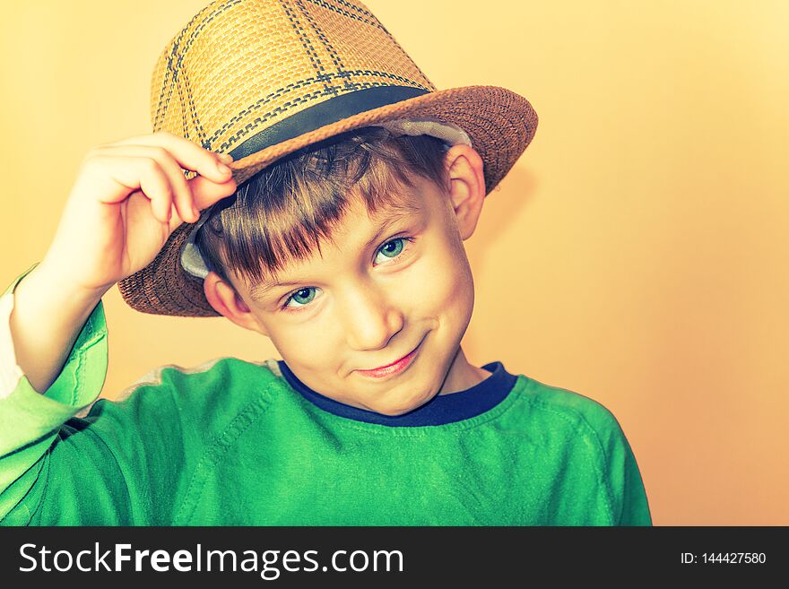 A Boy In A Straw Hat And A Green T-shirt Holding A Hat In A Sign Of Greeting