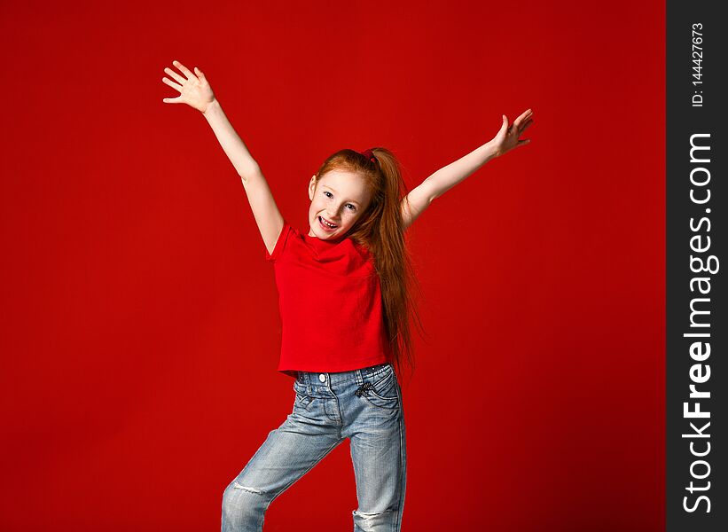 Portrait of a young girl with red hair smiling at camera with hands in the air isolated on red background