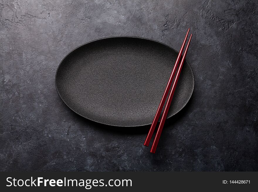 Empty plate and chopsticks over black textured table. Japanese food template. Top view with copy space. Flat lay
