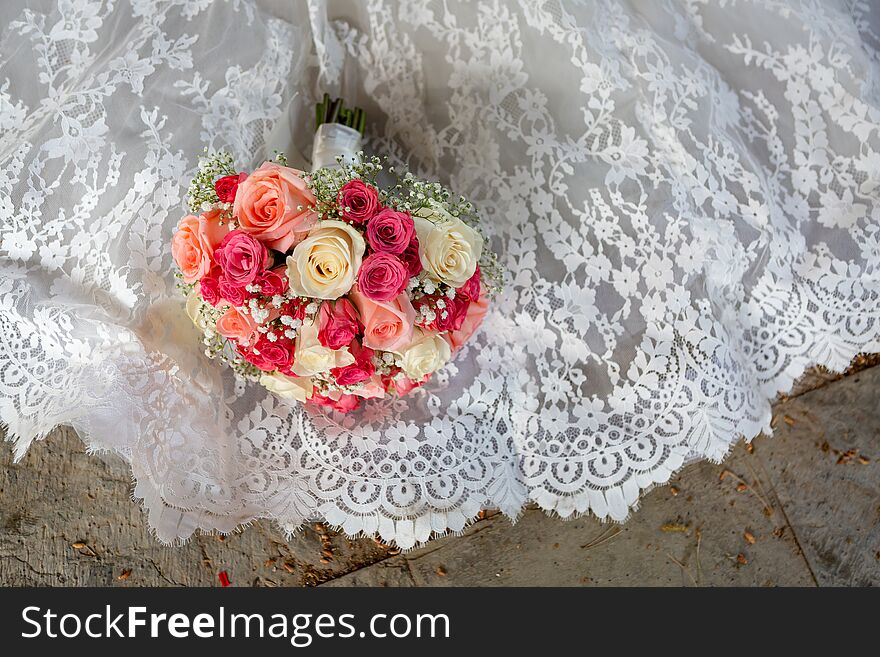 Wedding bouquet of colorful roses lying on a white wedding dress.