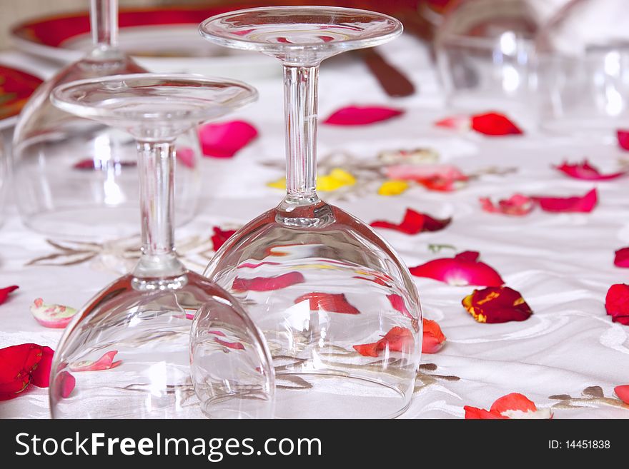 Glasses on a white tablecloth decorated with red flower petals. Shallow depth of field. Concept of celebration. Glasses on a white tablecloth decorated with red flower petals. Shallow depth of field. Concept of celebration.