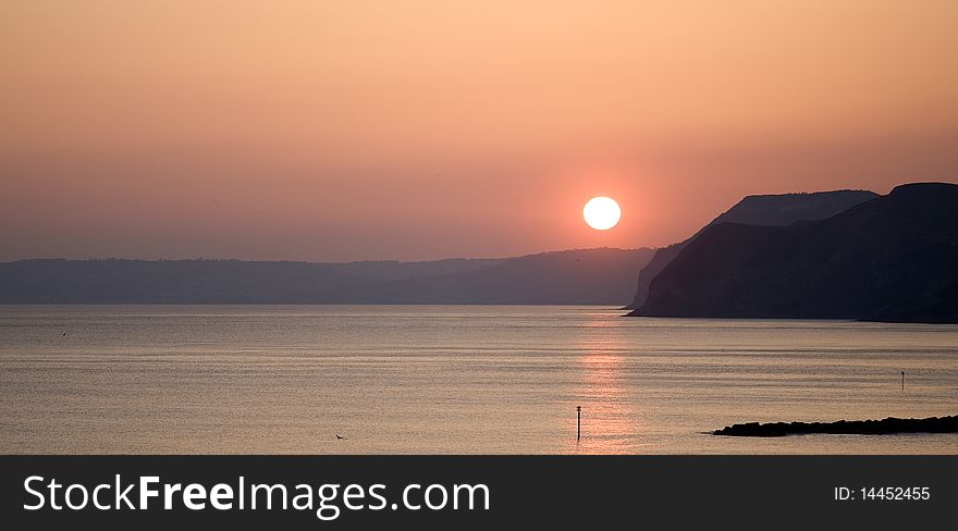 Panoramic shot of setting sun with reflections in ocean and cliffs in middle distance. Panoramic shot of setting sun with reflections in ocean and cliffs in middle distance.