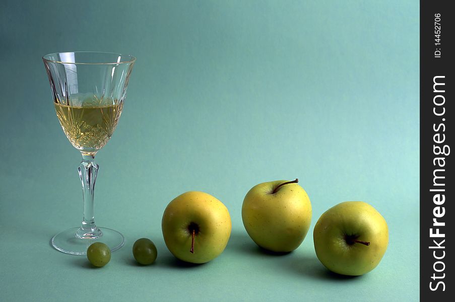 A glass of white wine with fruits isolated on green background. A glass of white wine with fruits isolated on green background