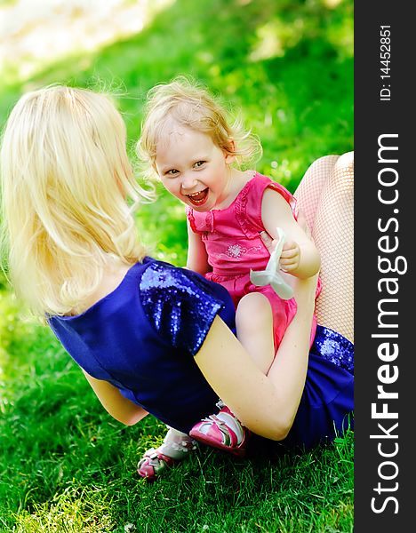 Cute girl sits with her mother on green grass and laugh. Cute girl sits with her mother on green grass and laugh