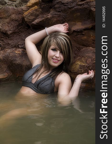 A pretty woman is sitting against the rocks on a pool relaxing. A pretty woman is sitting against the rocks on a pool relaxing.