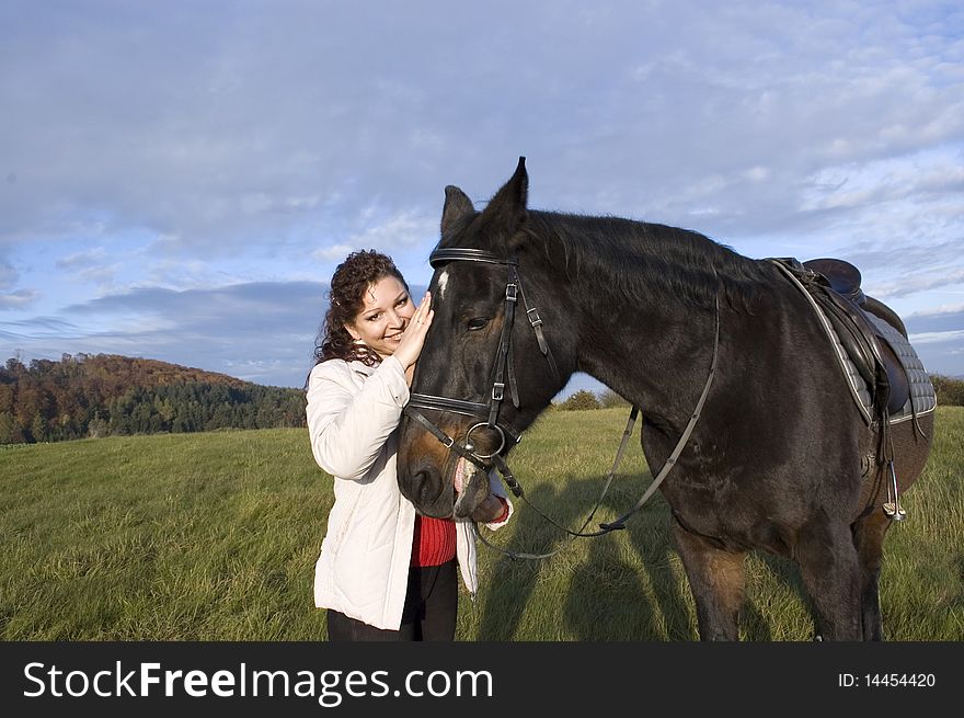 The woman and the horse stand on a background of the sky and field. The woman and the horse stand on a background of the sky and field.