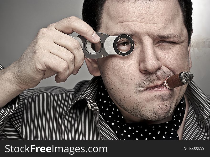 Handsome man smoking a cigar and looking through a cigar clipper. Handsome man smoking a cigar and looking through a cigar clipper.