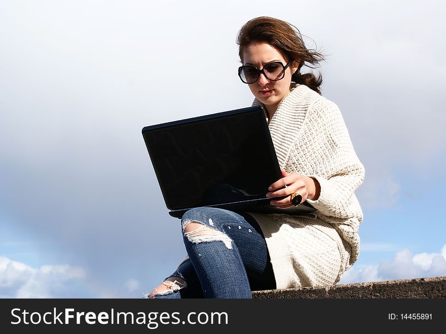 Young woman working with laptop on the beach . Wearing sunglasses and cotton coat . Windy day . Young woman working with laptop on the beach . Wearing sunglasses and cotton coat . Windy day .