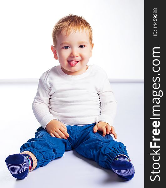Cute happy baby sitting on the floor and showing tongue