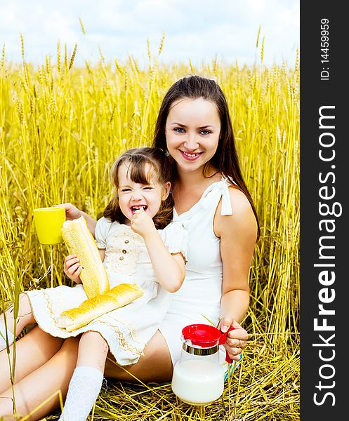 Happy mother and her little daughter having a picnic in the wheat field