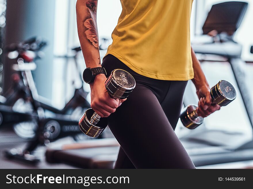 Close-up on a hands with dumbbells. Fitness girl trains in the modern gym.