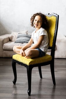 A Pretty Cute Little Girl With Curly Hair Sitting On The Chair And Smiling Stock Photography