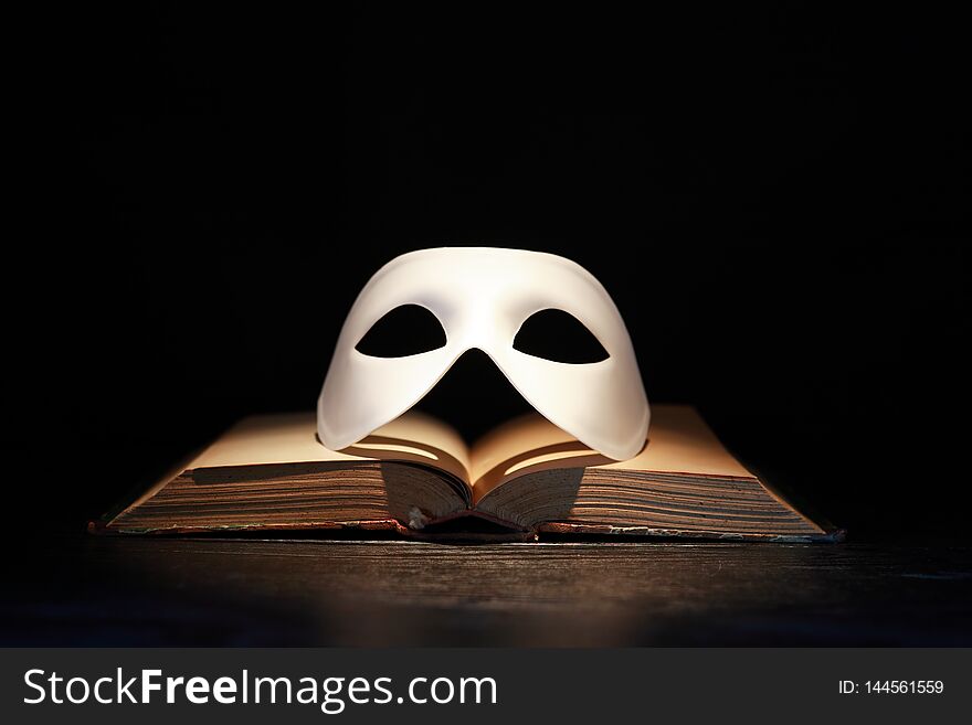 Classical white Venetian mask on old book against dark background. Classical white Venetian mask on old book against dark background