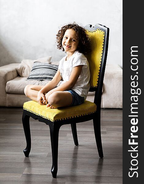 A pretty cute little girl with curly hair sitting on the chair and smiling