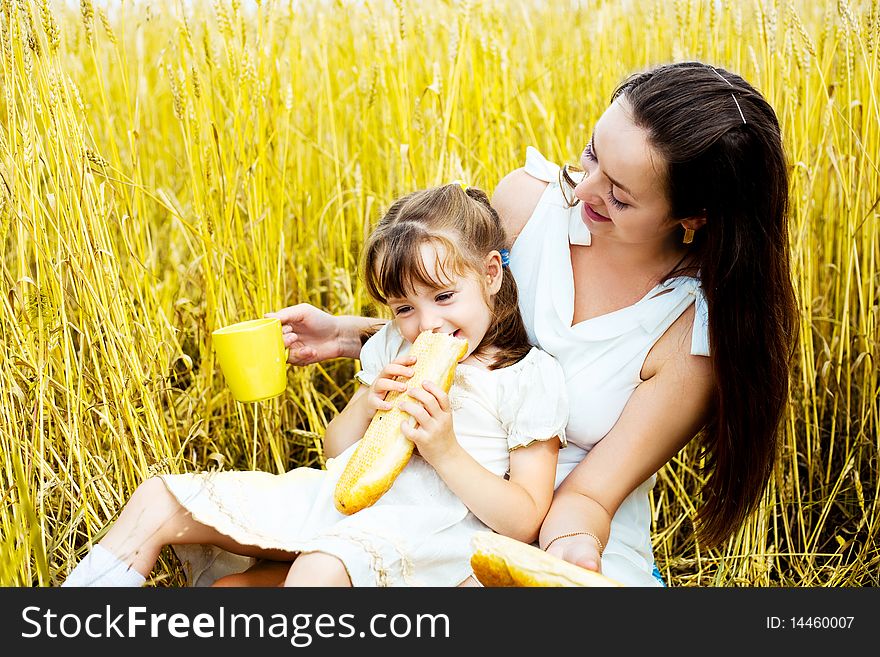 Happy mother and her  little daughter having a picnic  in the wheat field