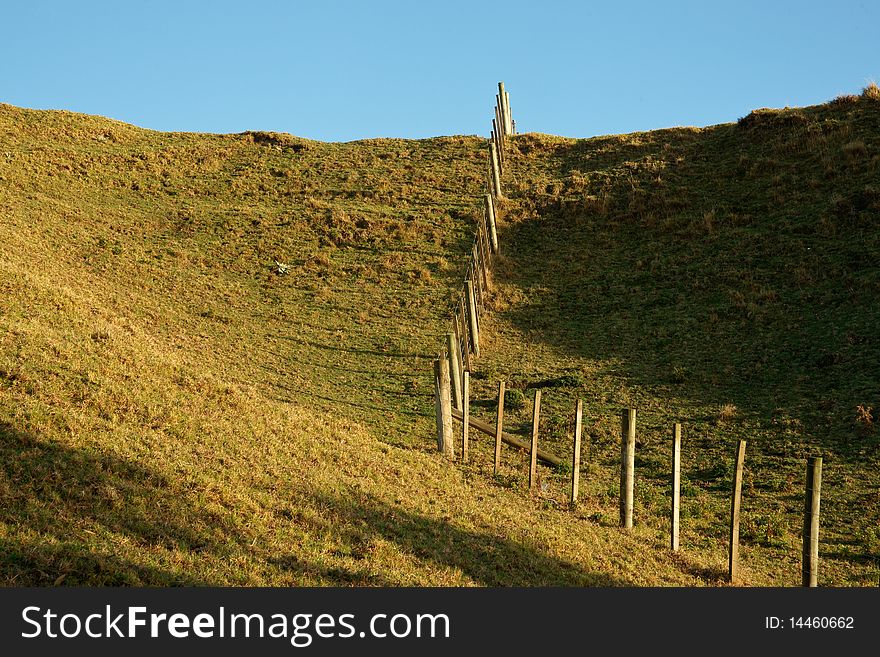 Fence running uphill, disecting fields under blue sky. Fence running uphill, disecting fields under blue sky.