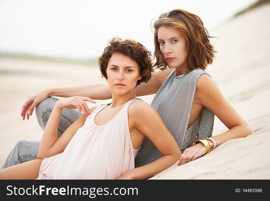 Two Fashionably Dressed Attractive Young Women Laying Amongst Sand Dunes. Two Fashionably Dressed Attractive Young Women Laying Amongst Sand Dunes