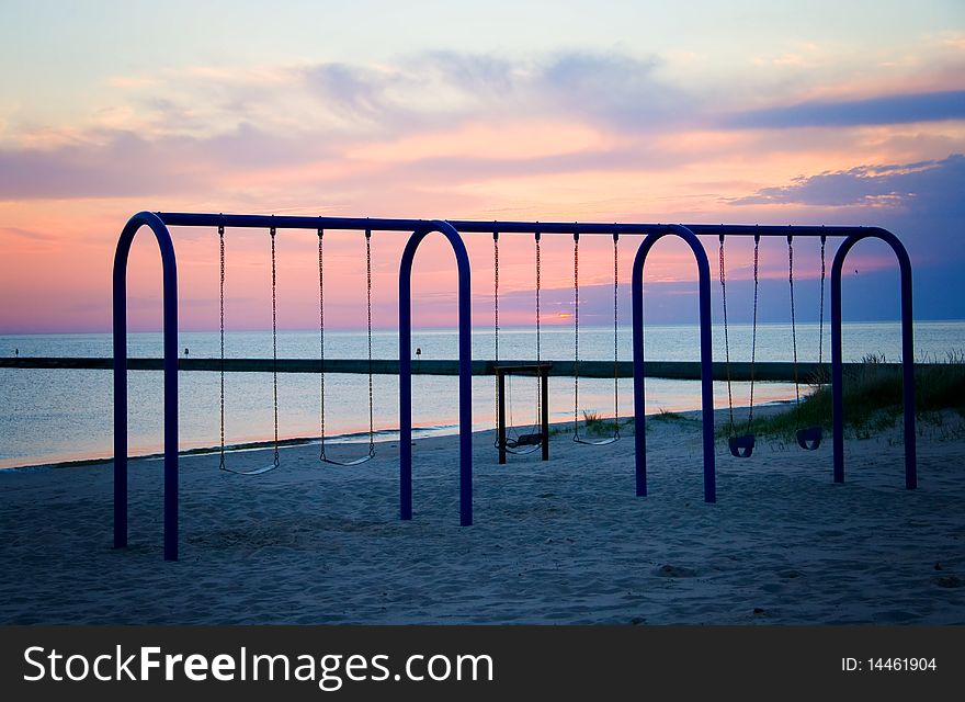 The swing set on the beach in Frankfort, Michigan is silhouetted against the sunset. The swing set on the beach in Frankfort, Michigan is silhouetted against the sunset.